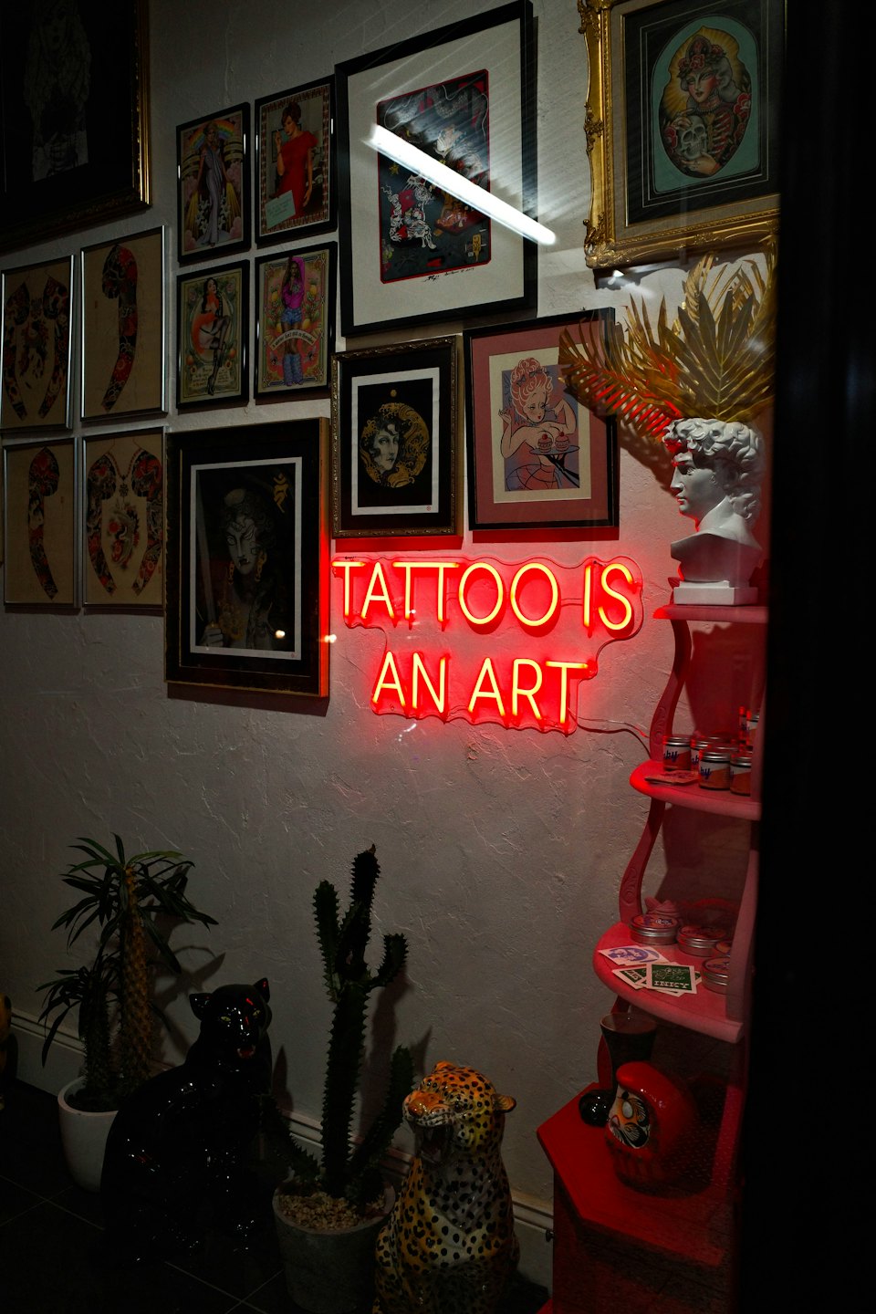 Wanddekoration in einem Tattoostudio mit gerahmten Kunstwerken und einem Neonschild.